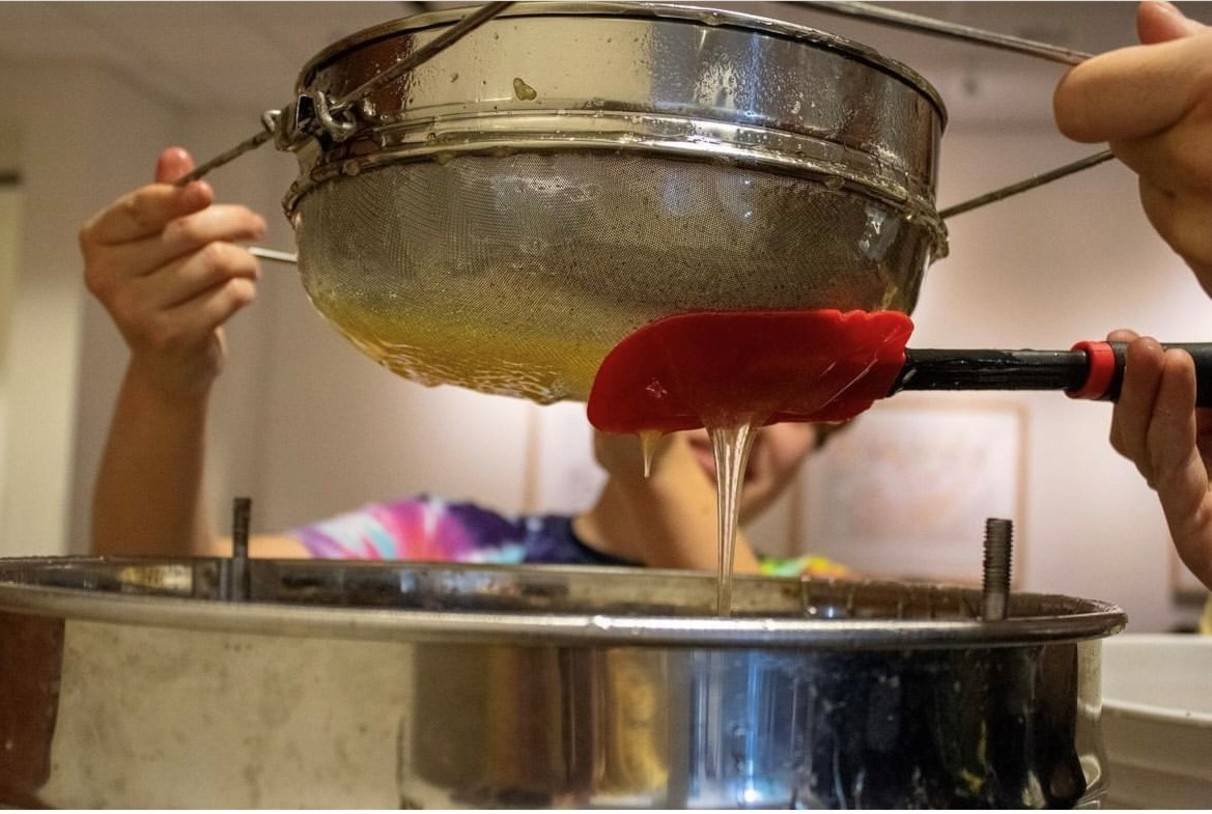 honey being strained over a large steel pot